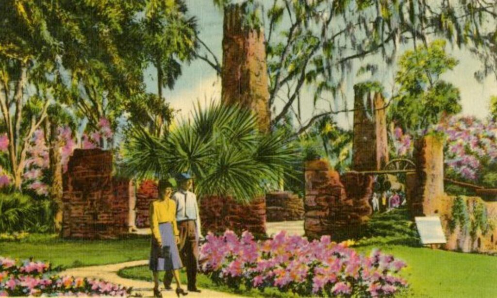 Vintage Florida postcard showing visitors strolling through lush gardens surrounding old sugar mill ruins, with blooming azaleas, palmettos, brick arches, and towering chimneys under draping Spanish moss. This romantic Old Florida setting reflects the historic landscapes that continue to shape Volusia County’s cultural heritage and inspire writers drawn to nature, memory, and place.