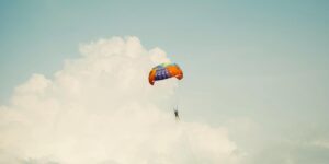 A stylized photo of a parasailor suspended beneath a bright multicolored parachute. He drifts against towering summer clouds, capturing the adventurous coastal recreation and skyborne views that define Florida’s beaches and continue to inspire writers exploring Volusia County’s landscape and creative culture..